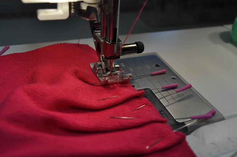 Nähmaschine näht die Falten der Kräuselärmel an einem pinken Shirt