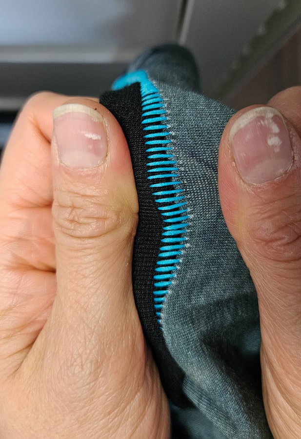 Detail einer türkisfarbenen Flachnaht Overlock am schwarzen Halsbündchen eines Shirts.