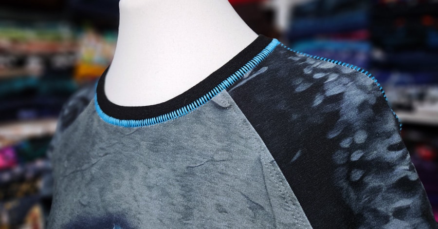 Halsausschnitt eines Shirts mit schwarzem Bündchen und dekorativer türkisfarbener Flachnaht Overlock.