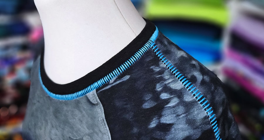 Detail von Halsausschnitt und Raglanärmel mit türkisfarbener Flachnaht Overlock am fertigen Shirt.
