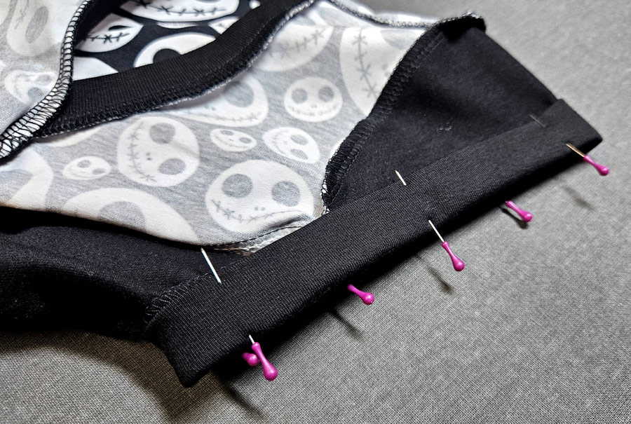 Der Ärmelsaum eines Shirts wird mit Stecknadeln für die Wave-Flachnaht fixiert.