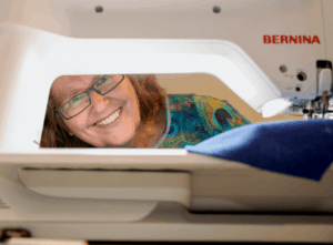 Lächelnde Kursteilnehmerin blickt durch den Freiarm einer Bernina-Nähmaschine während eines Courleys Nähkurses.