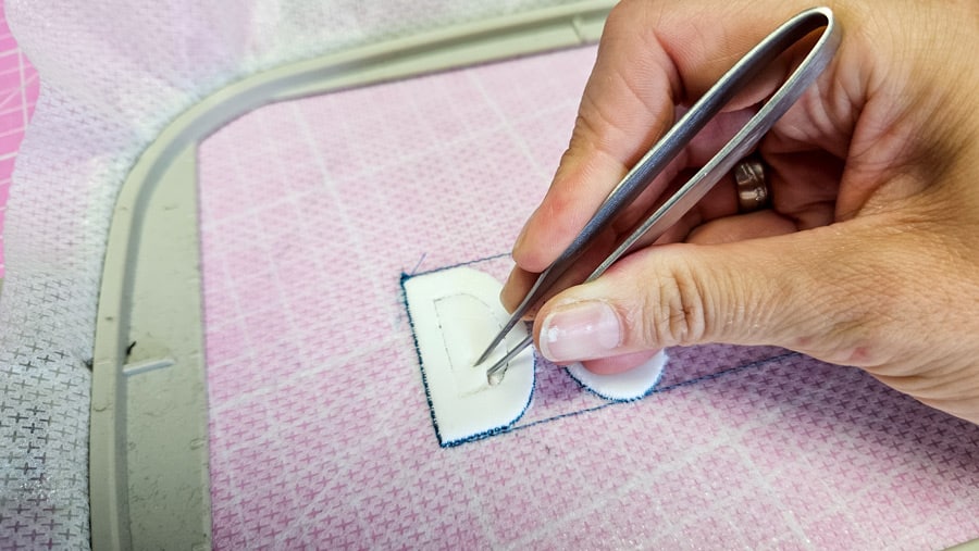 Überschüssiger Stickschaum wird mit einer Pinzette aus der Trapunto-Stickerei entfernt.