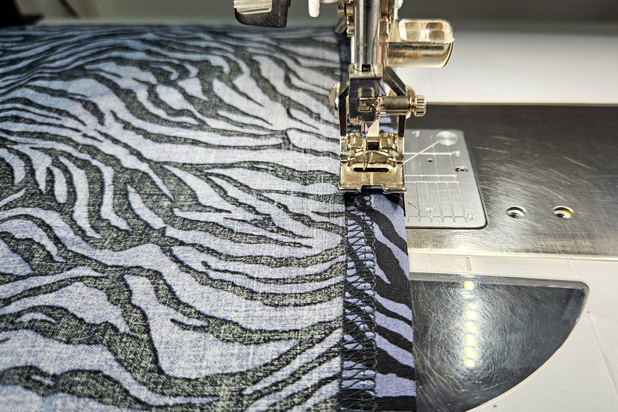Stoffkante eines Ärmels aus Viskose wird vor der weiteren Verarbeitung mit der Overlock versäubert.