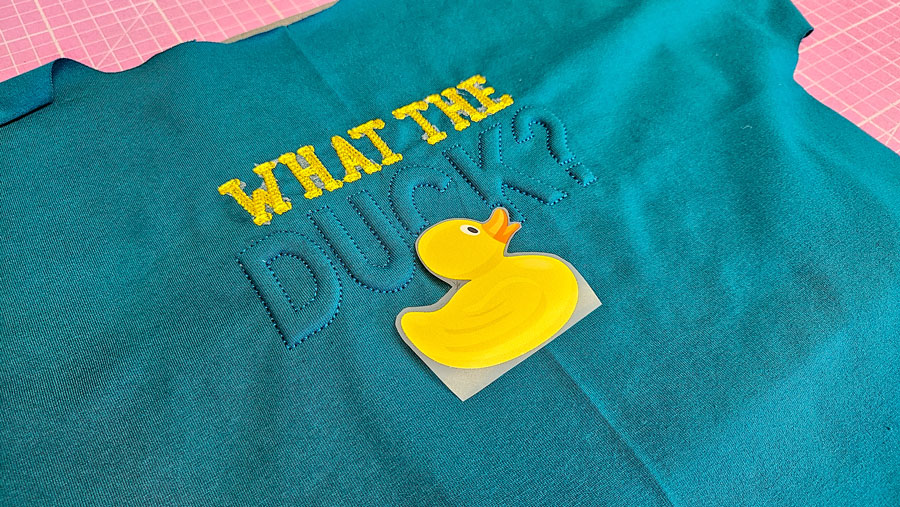 Gelbes Enten-Bügelbild wird unterhalb der Trapunto-Stickerei auf dem Shirt-Vorderteil positioniert.