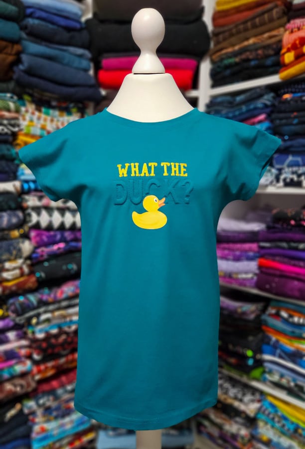 Fertiges türkisfarbenes Kindershirt mit plastischer Trapunto-Stickerei, gelber Schrift und Entenmotiv.