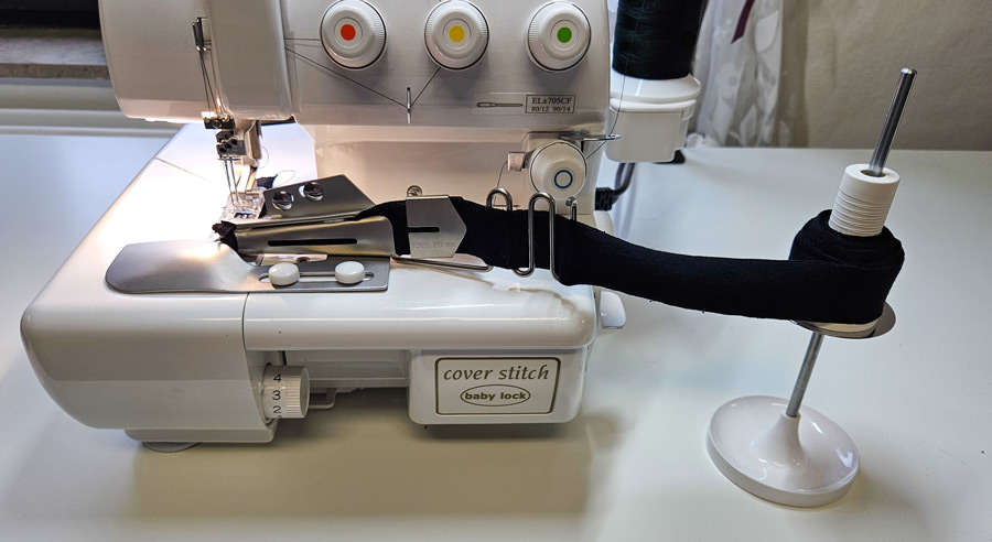Aufgerollter schwarzer Einfassstreifen wird neben einer Coverstitch zum Einfasser geführt