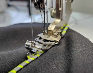 Die Kapuzennaht wird neben der Reflektorpaspel mit Reflektorgarn im Deckstich abgesteppt.